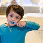Niño pequeño cepillándose los dientes con ayuda de su madre, como parte de una rutina dental saludable.