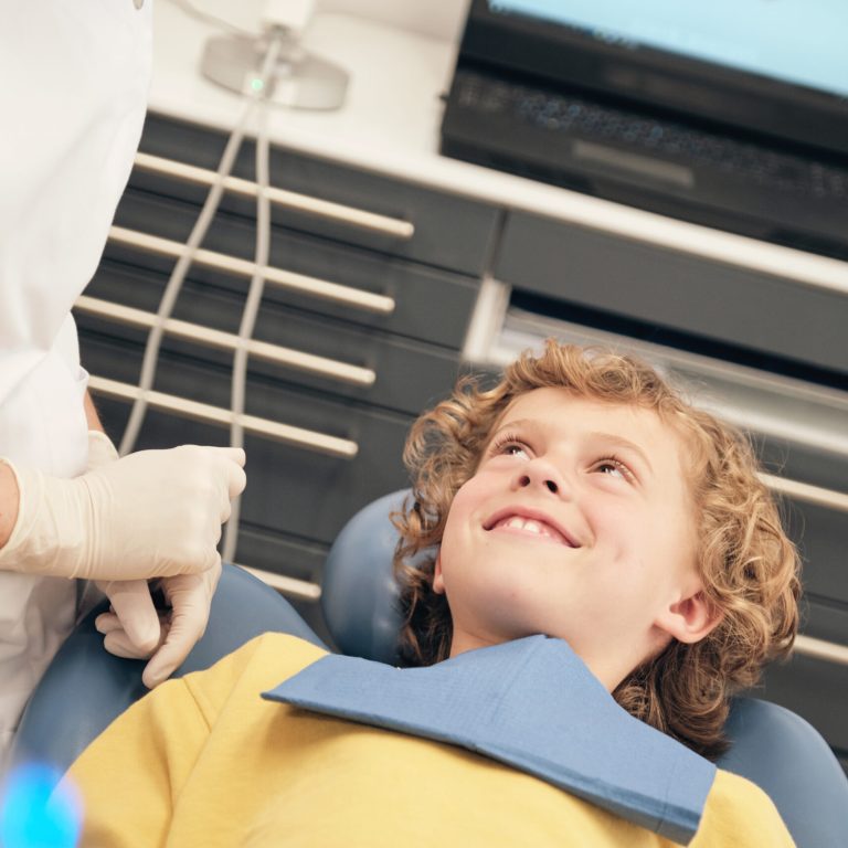 Adult woman in doctor uniform speaking to little patient in dentist office