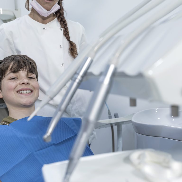 A cute boy is being examined by a professional pediatric dentist. Very happy boy after the visiting of doctor at the clinic with beautiful white smiles. Copy space.