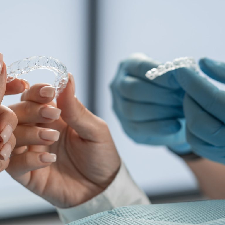 The hands of the doctor and the patient hold the veneers close-up. The dentist offers dental correction with transparent and discreet veneer aligners at the medical center. High quality photo